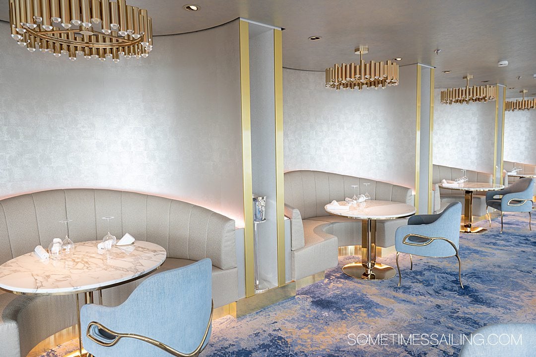 Interior of Enchante restaurant on Disney Wish cruise ship, with blue carpet and white details, and gold detailing, with seats facing the cruise ship windows.
