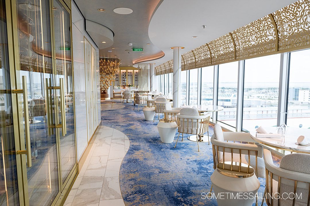 Interior of Enchante restaurant on Disney Wish cruise ship, with blue carpet and wavy white details, and gold detailing, with seats facing the cruise ship windows.