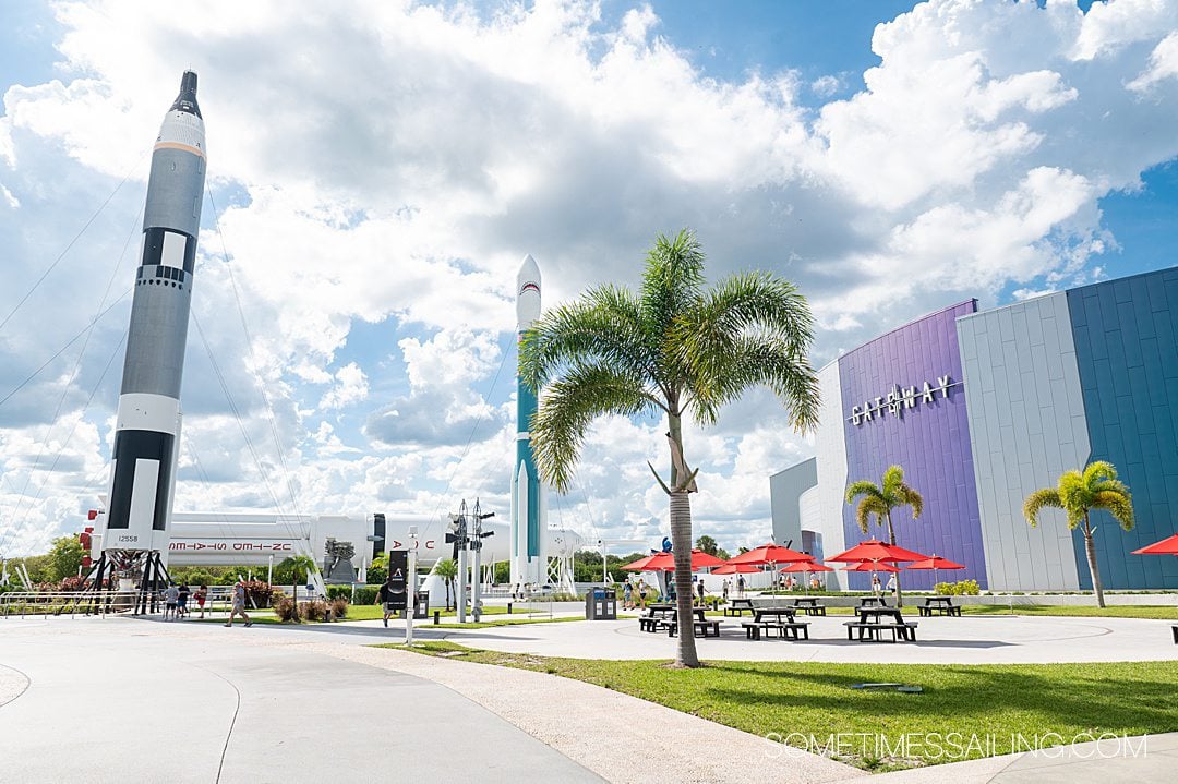 Inside the Kennedy Space Center Complex, with rockets, palm trees and a purple Gateway building, near Port Canaveral.