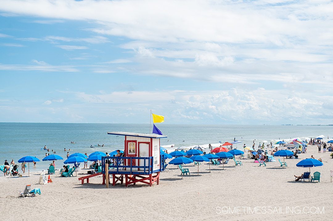 Cocoa Beach shore with blue umbrellas and a small red and white lifeguard stand.