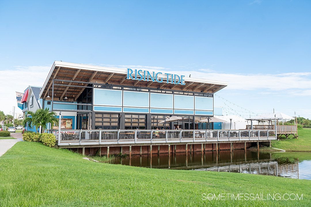 Outside of a restaurant with Rising Tide in letters on top with green grass and a blue sky.