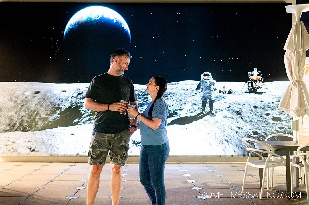 Couple cheersing glasses and looking at each other in front of a mural of an astronaut on the moon behind them at The Space Bar in Titusville near Port Canaveral.