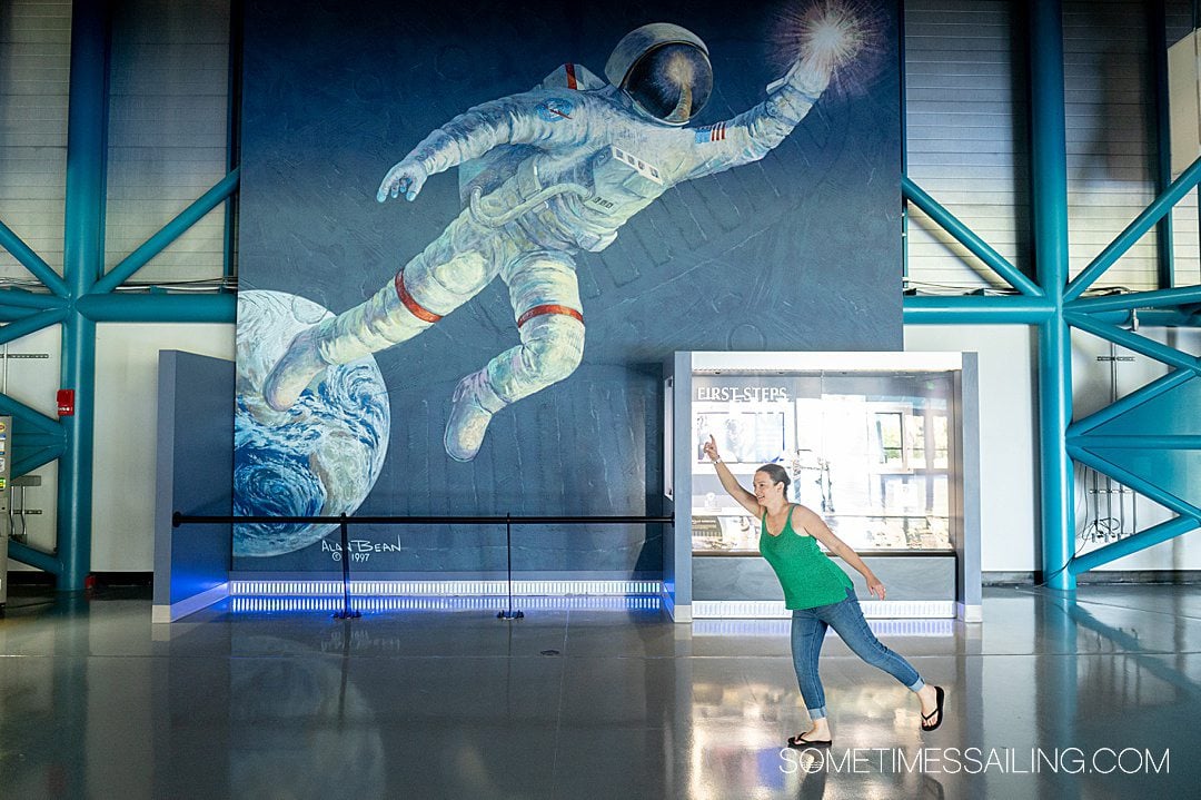 A mural of an astronaut at Kennedy Space Center in the Apollo/Saturn V building, with a woman posing in the lower right corner.