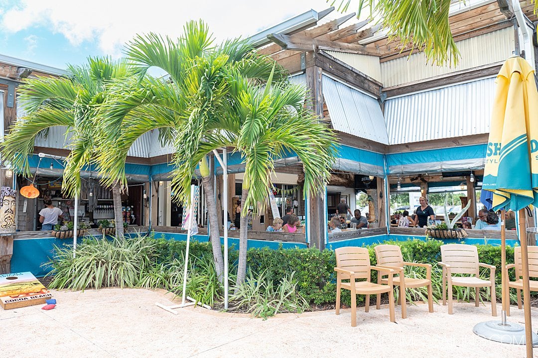 Exterior of a restaurant's outdoor seating area with palm trees.