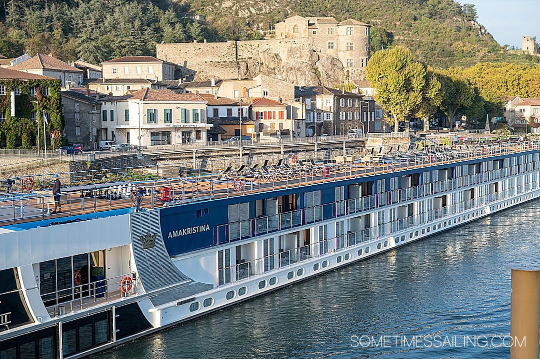 AmaWaterways AmaKristina cruise ship in the water with a castle behind it on a hill in Tournon, France.