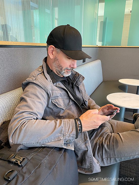 Man looking at his phone with a gray jacket on and black hat, and bracelets on his wrist.