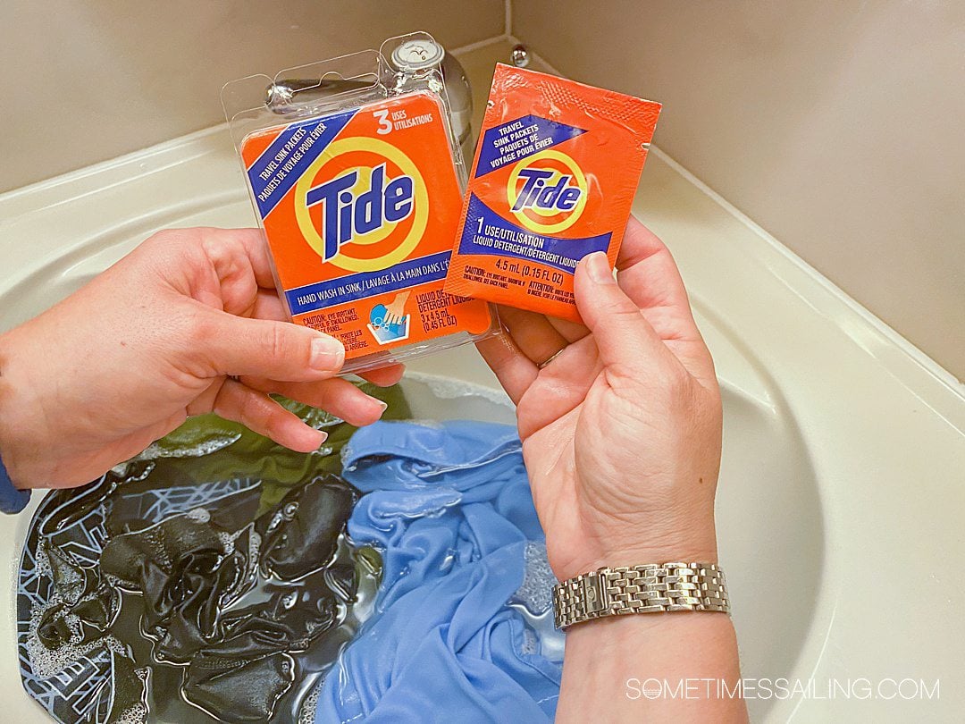 Orange travel Tide laundry detergent packs above a sink filled with clothes and water.