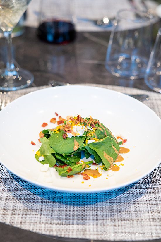 Spinach salad with dressing, bacon pieces and egg on top.