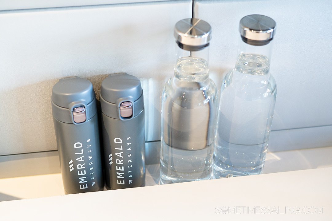 Two glass bottles of water next to two gray reusable water bottles on a tabletop.