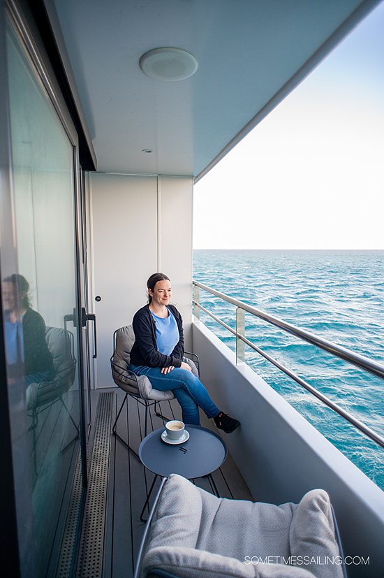 Woman on the balcony of a stateroom on Emerald Azzurra yacht cruise ship with a cup of coffee looking out to the ocean.