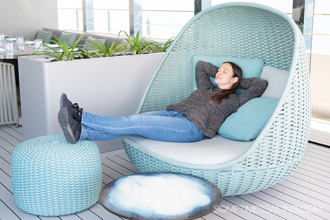 Aqua daybed lounge chair on the outside deck of a cruise ship with a woman lying on it relaxing.