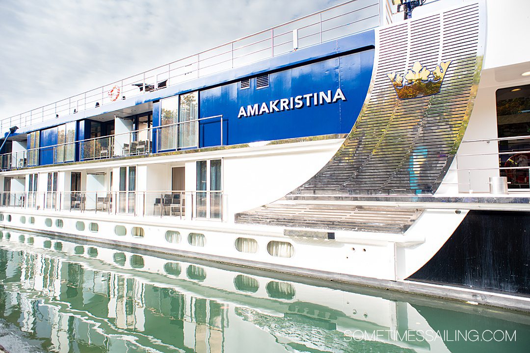 Exterior of AmaKristina river cruise ship with blue and white details, and the ship's reflection in the river water below.