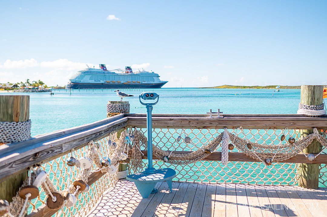 Disney Wish cruise ship in the background with a Castaway Cay deck with fish netting in the foreground in the Caribbean.