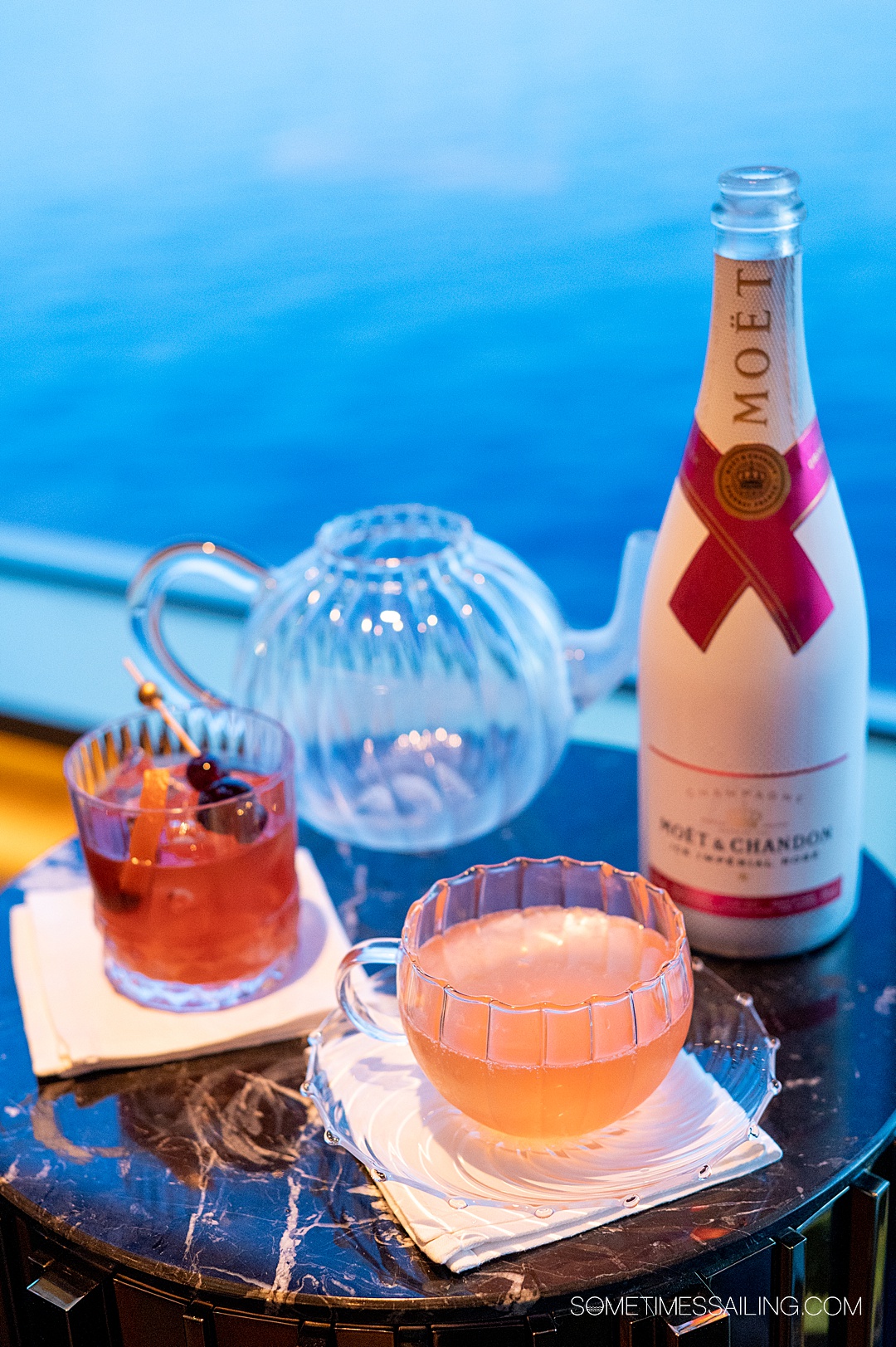 Table with cocktails and a bottle of champagne on the right during dusk, as adults-only on Disney Cruise Line.