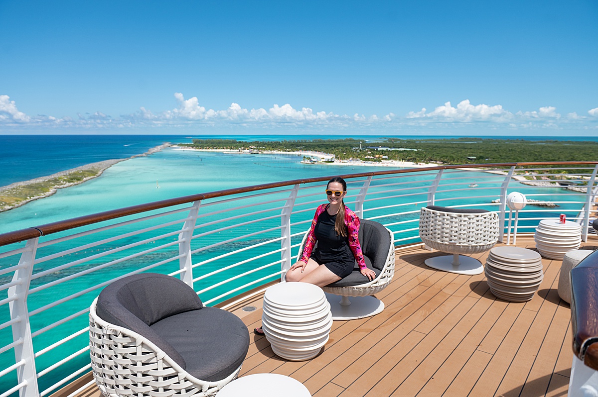 Woman sitting on a chair outside on a cruise ship overlooking the turquoise blue ocean.