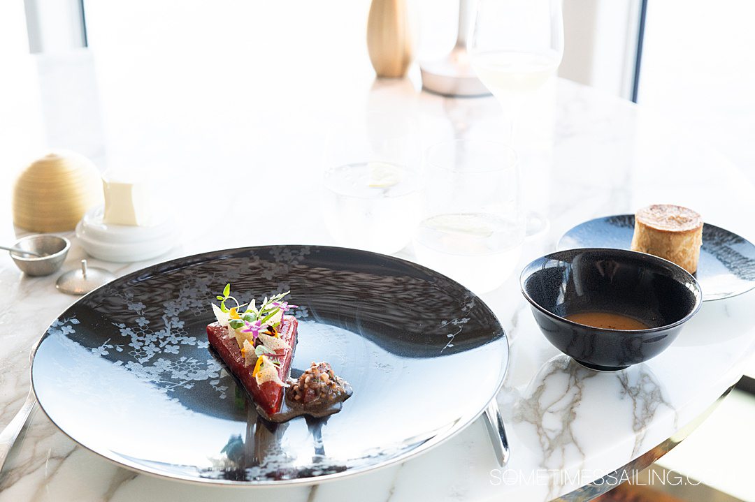 Marble table with a black plate, bowl, and bread plate on it.