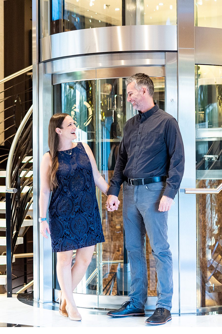 Couple standing together in front of a glass elevator near a sweeping staircase of an AmaWaterways river cruise ship.