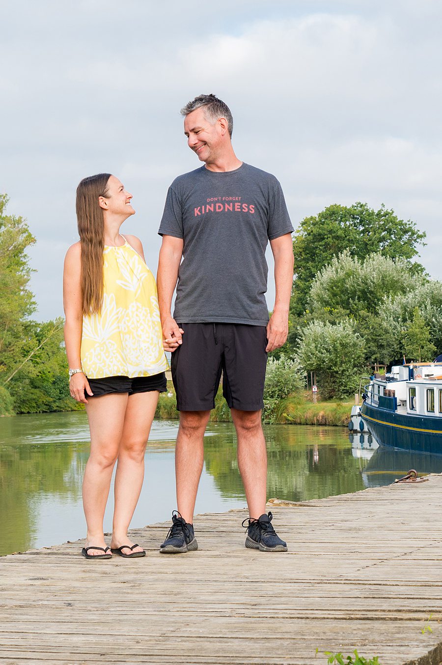 Couple looking at each other on a dock in front of a canal and barge cruise ship.