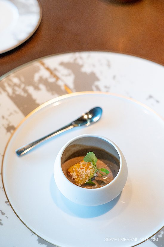 Small amuse bouche dish with a gnocchi dumpling in the middle of a small bowl, and small spoon on the plate.