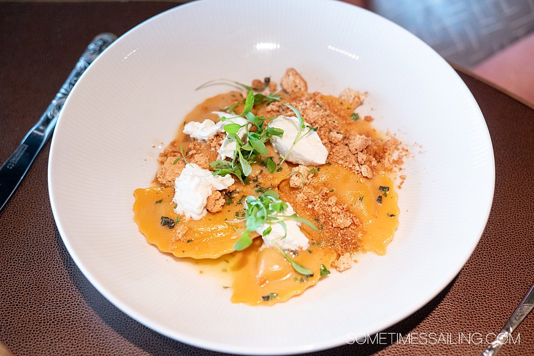 Entree with orange-colored ravioli and cheese on top with greens.