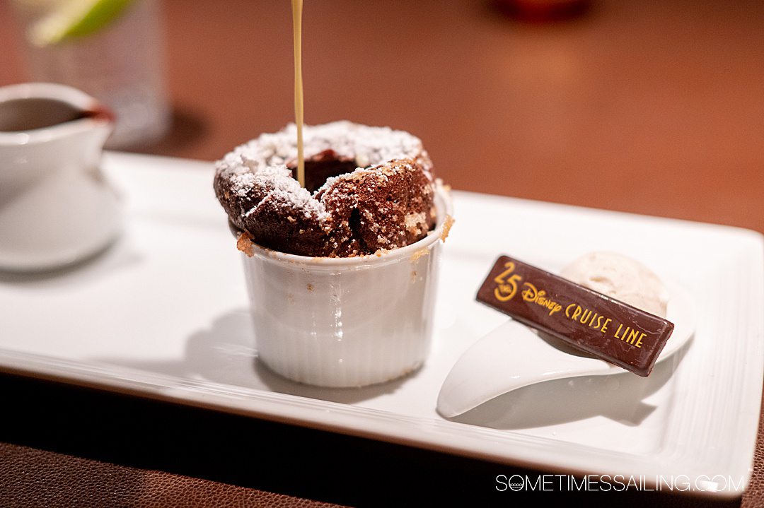 Chocolate souffle dessert with a piece of chocolate next to it and liquid chocolate being poured into it on a Disney Cruise.