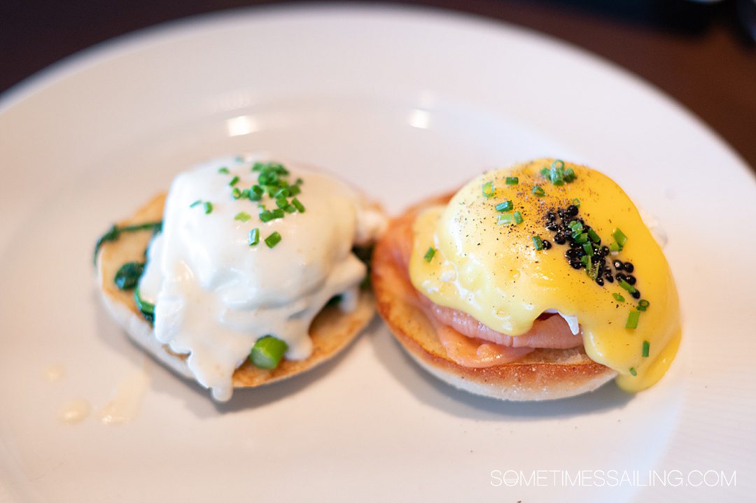 Two eggs Benedict halves on a white plate with white and yellow Hollandaise sauce.