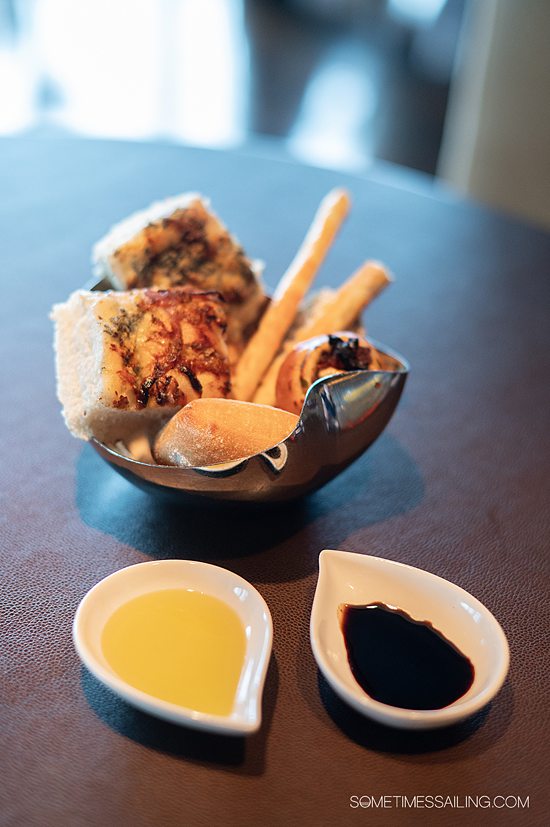 Braed basket with two tear-drop shaped white shallow dishes with oil and balsamic vinegar in them.