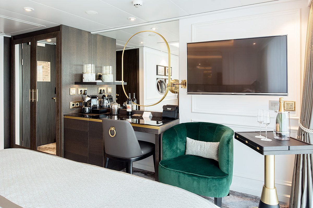 Inside a stateroom on Advance by Transcend Cruises, with a green velvet sitting chair and desk.