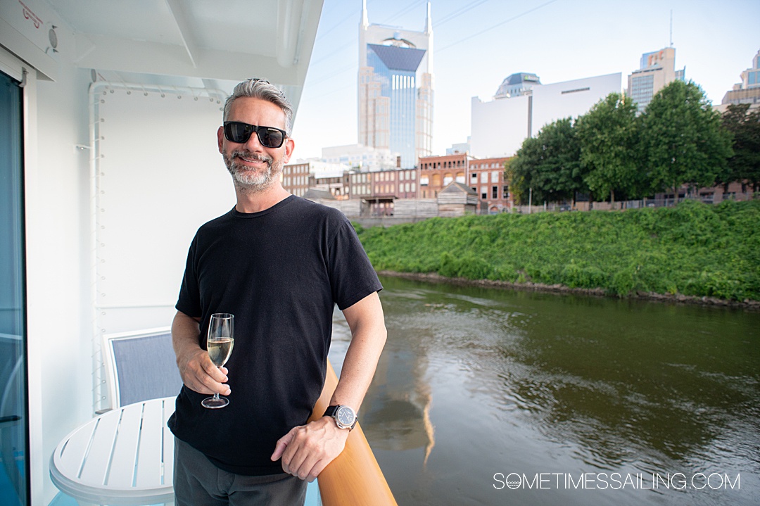 Man on a balcony of a Tennessee River cruise ship American Serenade with Nashville skyscrapers in the distance.