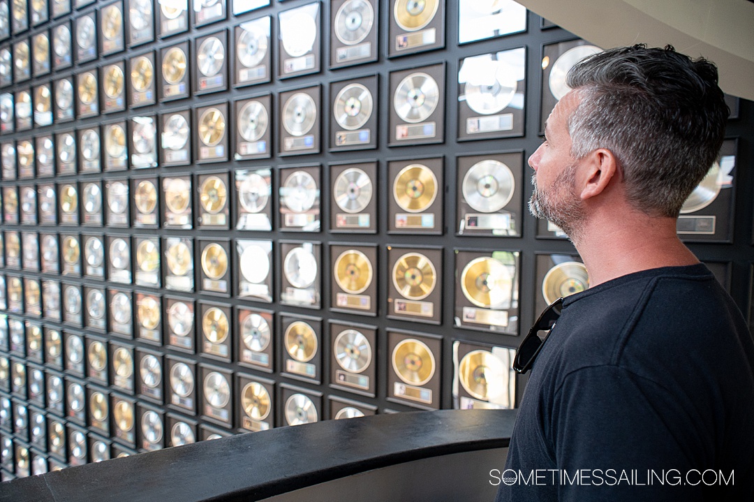 Wall of metallic framed records at the Country Music Hall of Fame with a man on the right looking at it.