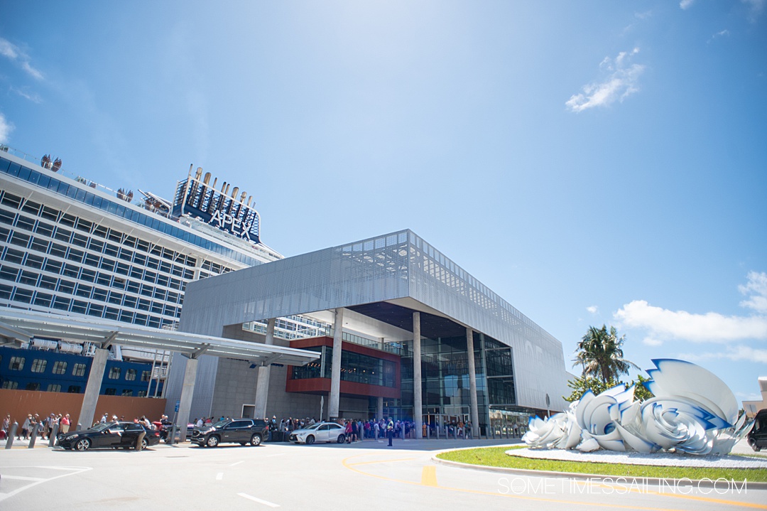 Exterior of a square cruise port terminal building with a cruise ship towering over it in the background at the Fort Lauderdale cruise port.