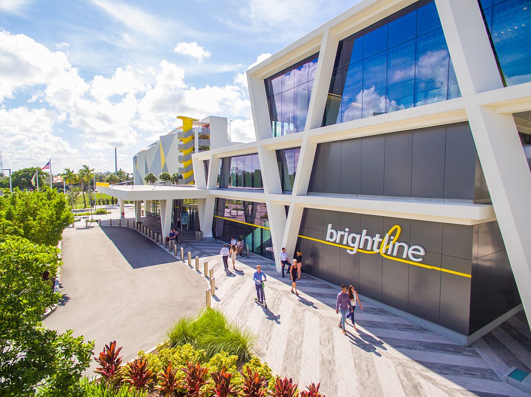 Exterior of the Brightline station in Fort Lauderdale on a sunny day with pedestrians walking by the front of the building.