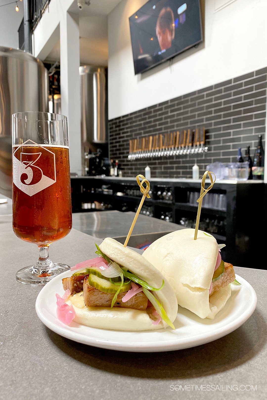 Plate on a counter with two bao buns and a glass of beer to the left at 3 Sons Brewery in Fort Lauderdale.