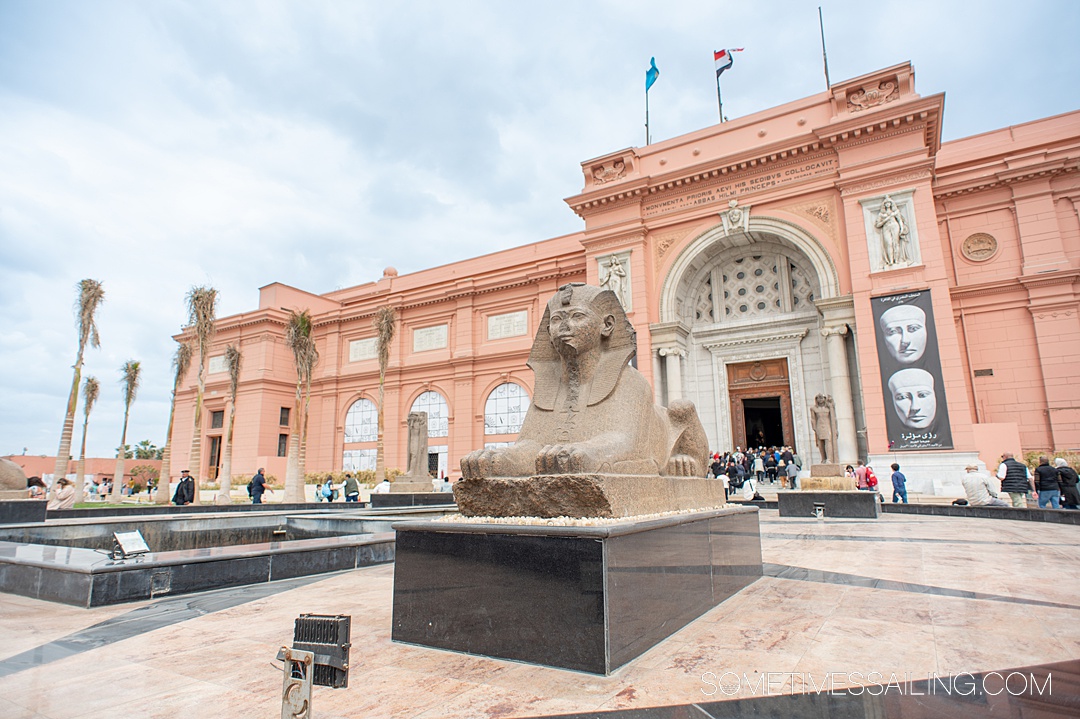 Peach colored facade of the Egyptian Museum with a Sphinx sculpture in front of it.