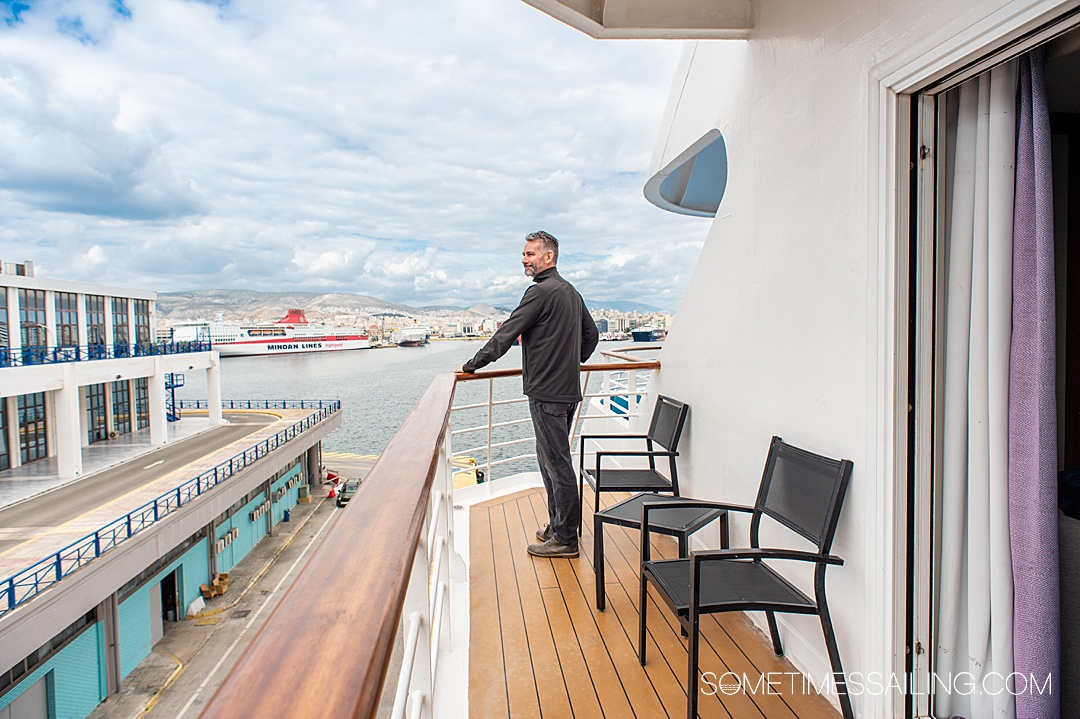 Man looking out from the balcony of a cruise ship room to the ocean and terminal at the cruise port in Athens.