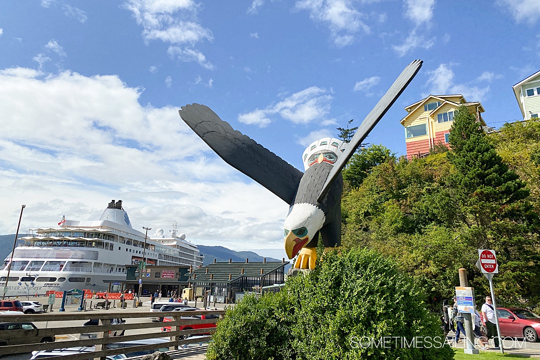 Wood-carved eagle sculpture with a cruise ship in the background on the left on a blue-sky day in Ketchikan. 