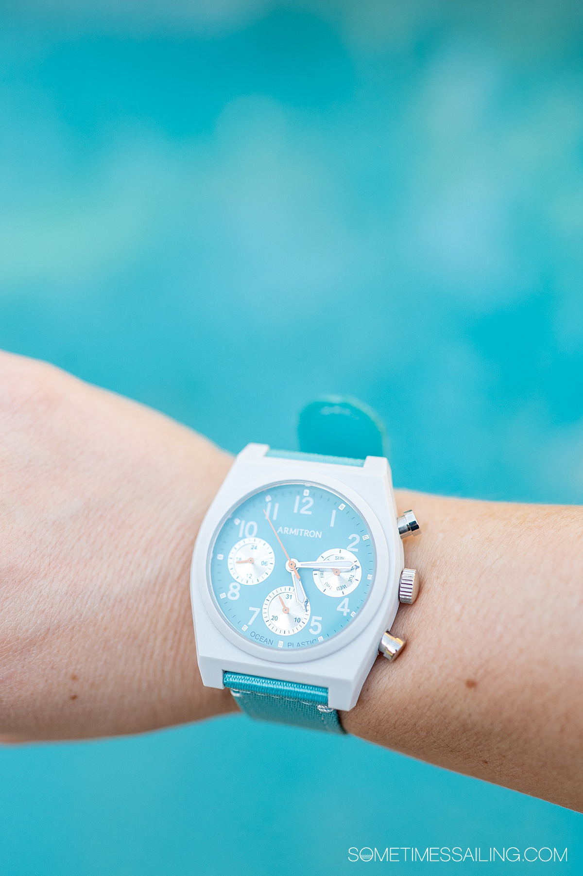 Light blue and white watch on a woman's writer, from Armitron watches, over a blue pool background.