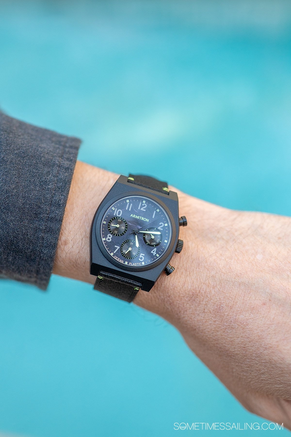 Black watch on a man's wrist, from Armitron watches, over a blue pool background.