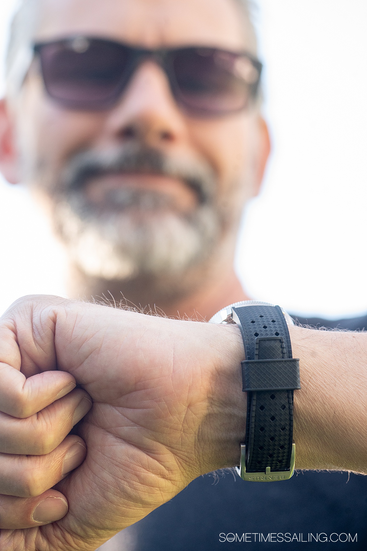 Man looks down at his wrist with a black watch band visible on the straps.