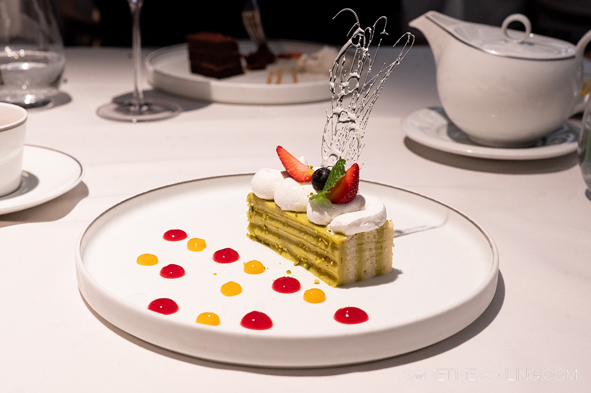 Dessert on a plate with fruit compote dots and a piece of cake with sugar art on top.