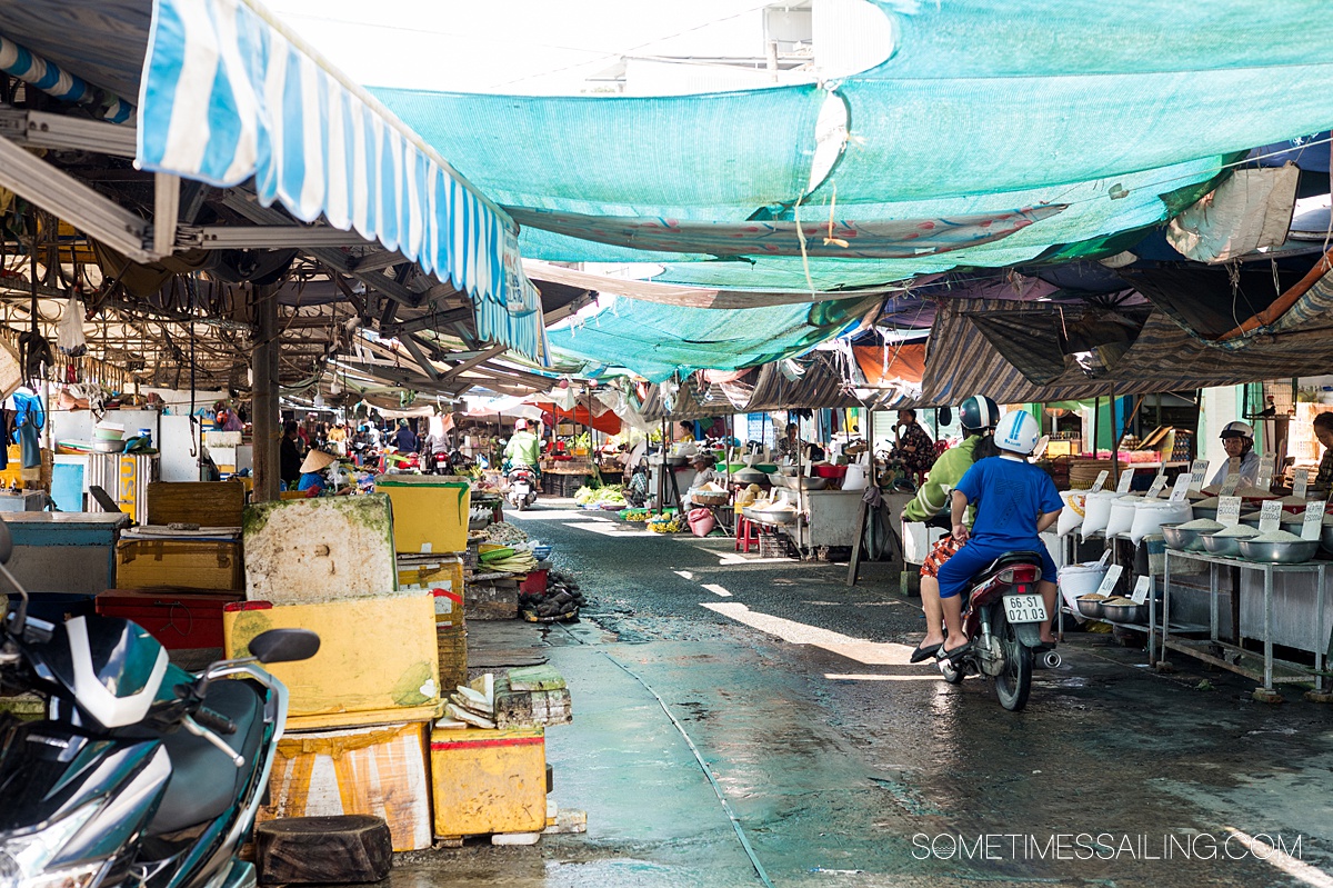 Market in Southeast Asia with various vendors on either side of a road and tarps for roof covering.