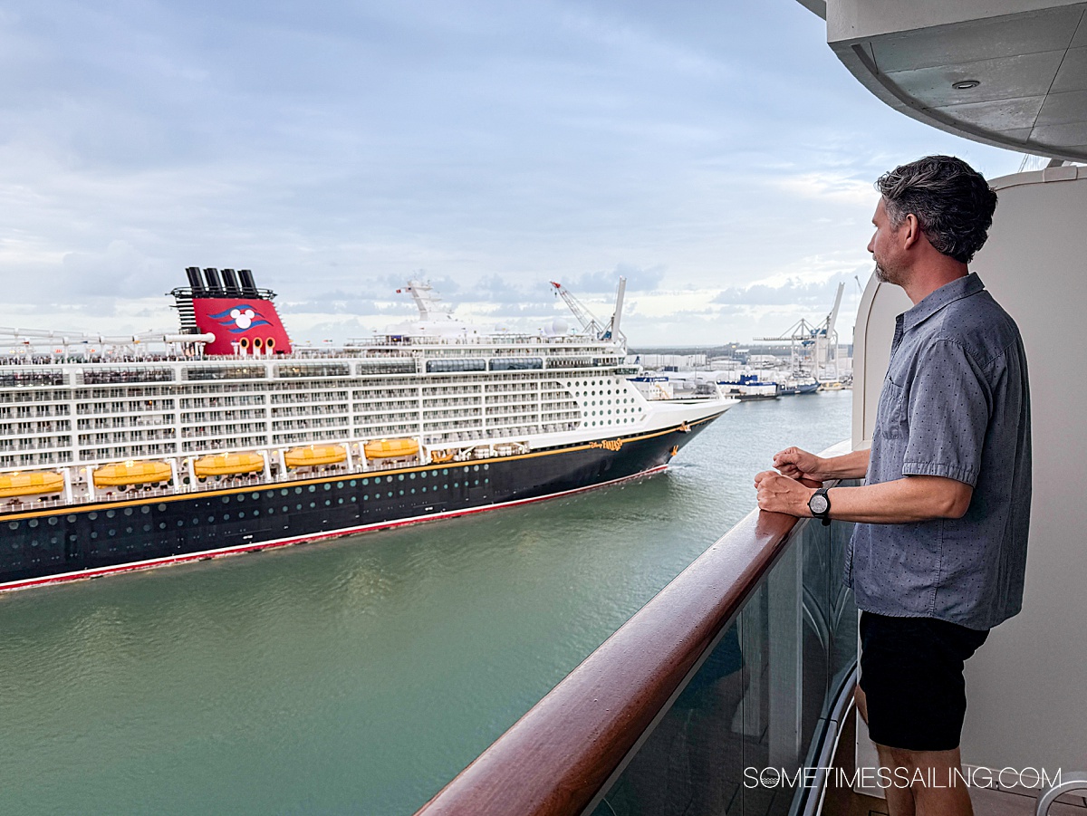 Man on the balcony of a cruise ship looking out to a Disney cruise ship passing by on the water.