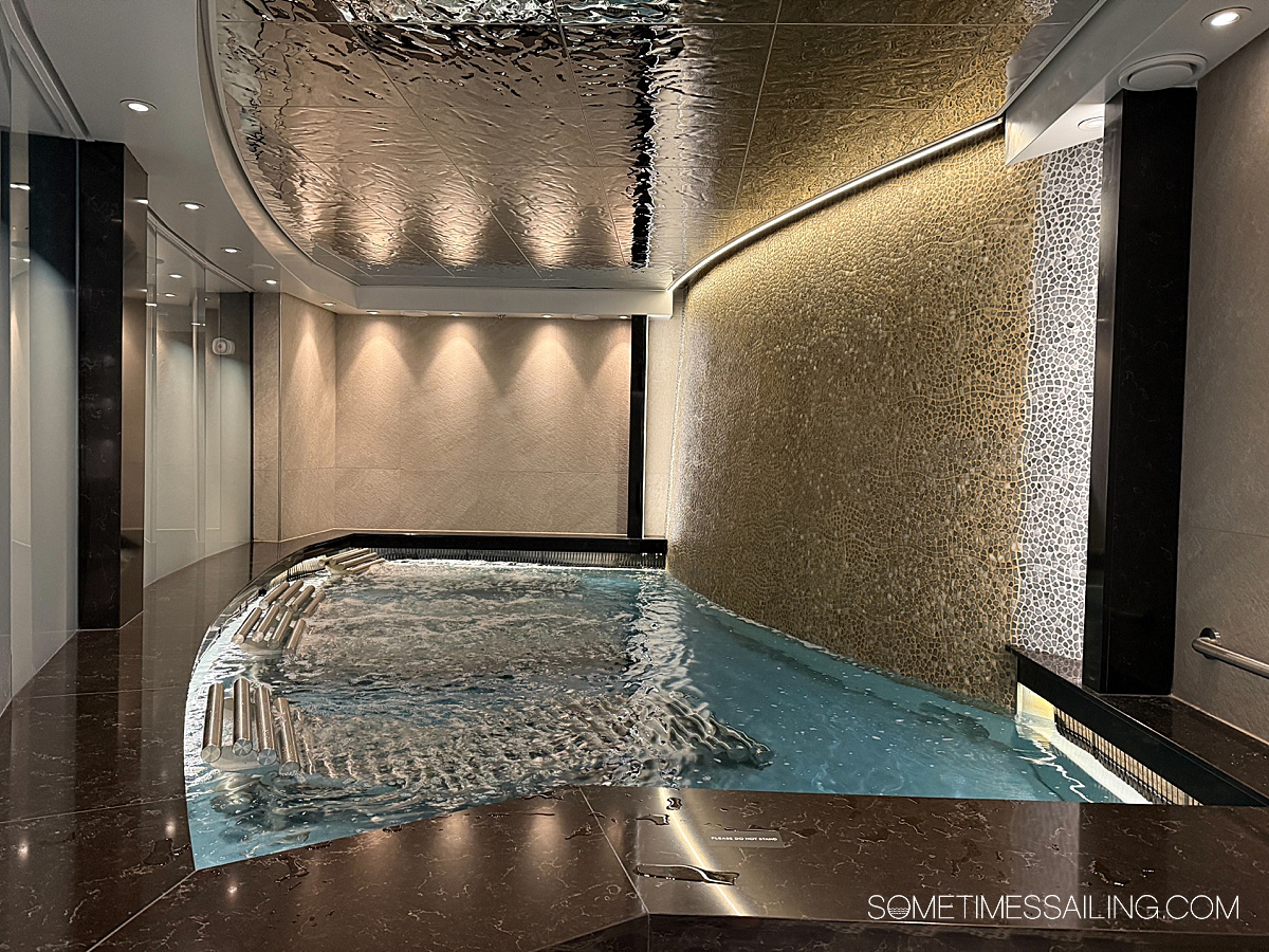 Hydra spa room on Celebrity Xcel cruise ship with a waterfall wall and metal lounge chairs in the water.