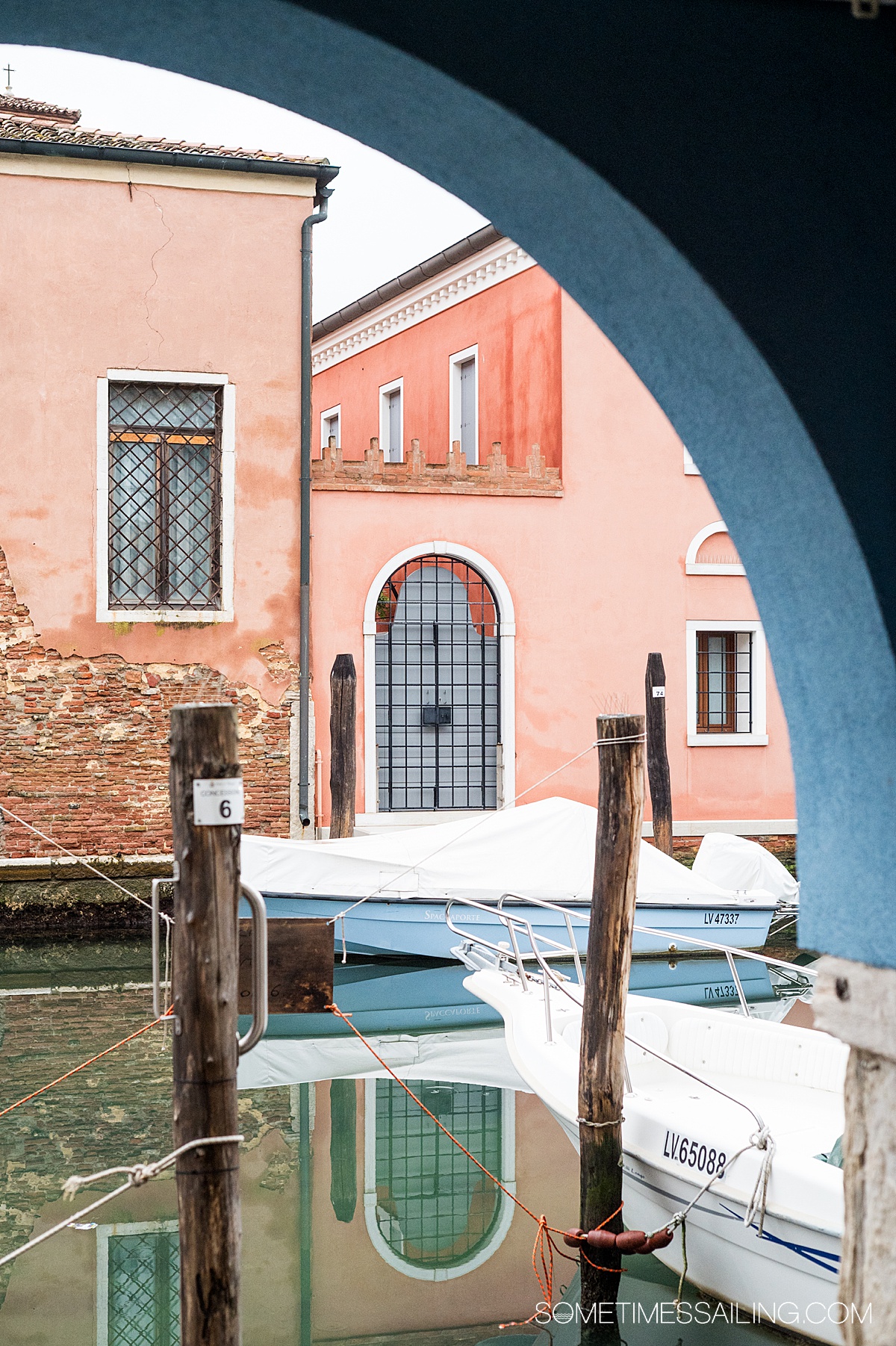 Navy blue archway reveals a beautiful canal scene with boats and pink buildings.