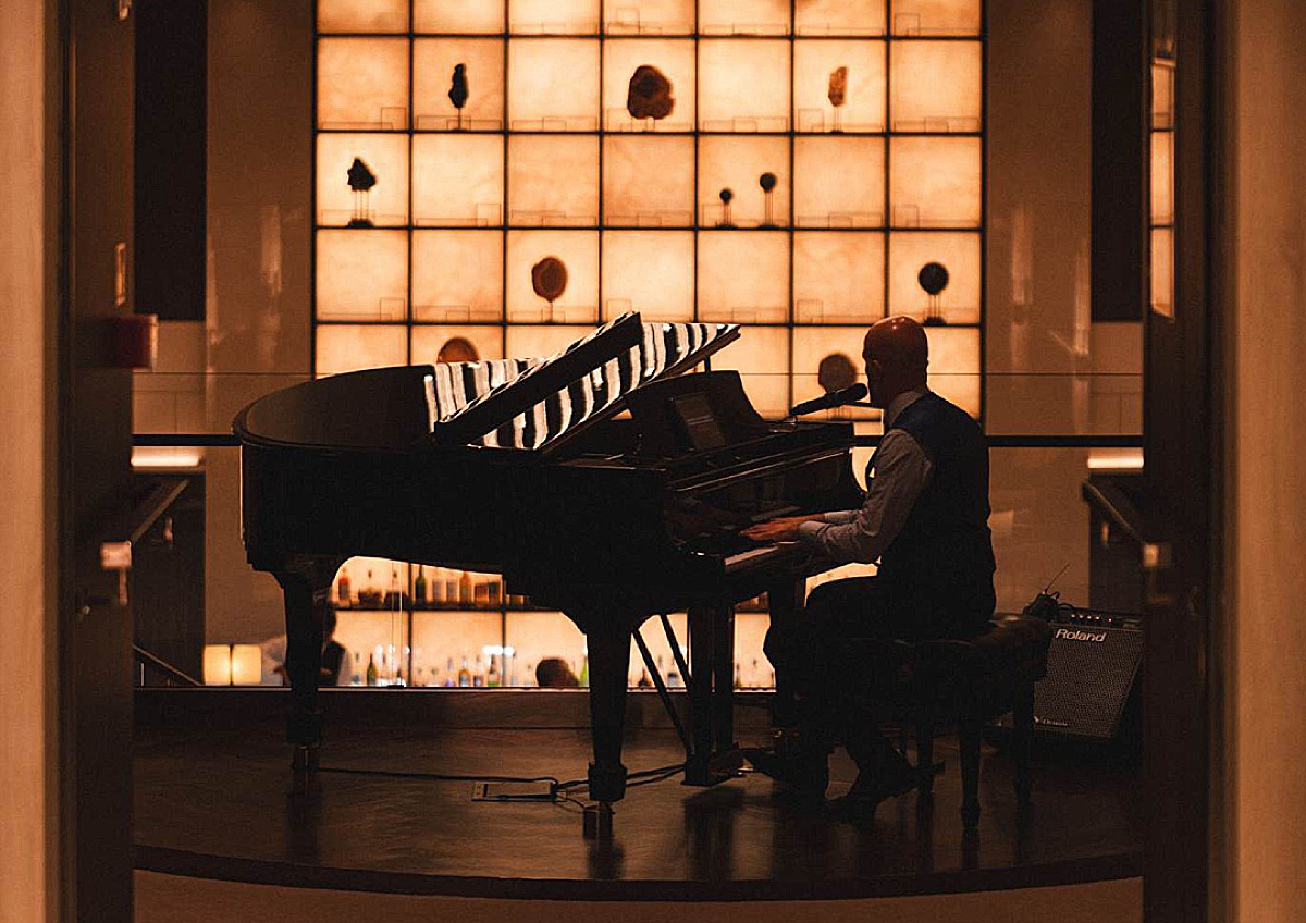 Silhouette of a man playing a black grand piano against an illuminated wall.