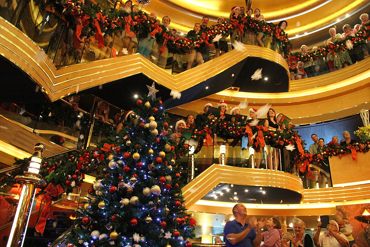 Looking up at several decks with Christmas carolers lining the balconies and a Christmas Tree with ornaments.