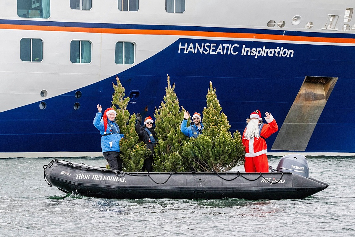 A Zodiac boat in the water in front of a cruise ship, with Christmas Trees and the crew with Santa Claus onboard.