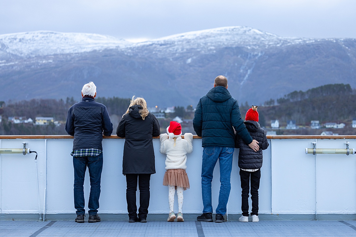 A family looks over the railing to the snow-capped mountains on a Hurtigruten cruise ship in Norway.