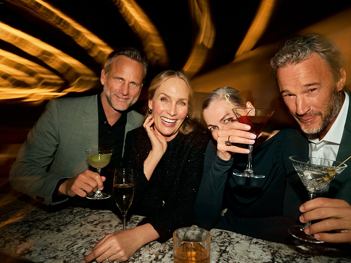 Four people at a bar with dim lights and festive cocktails in their hands.