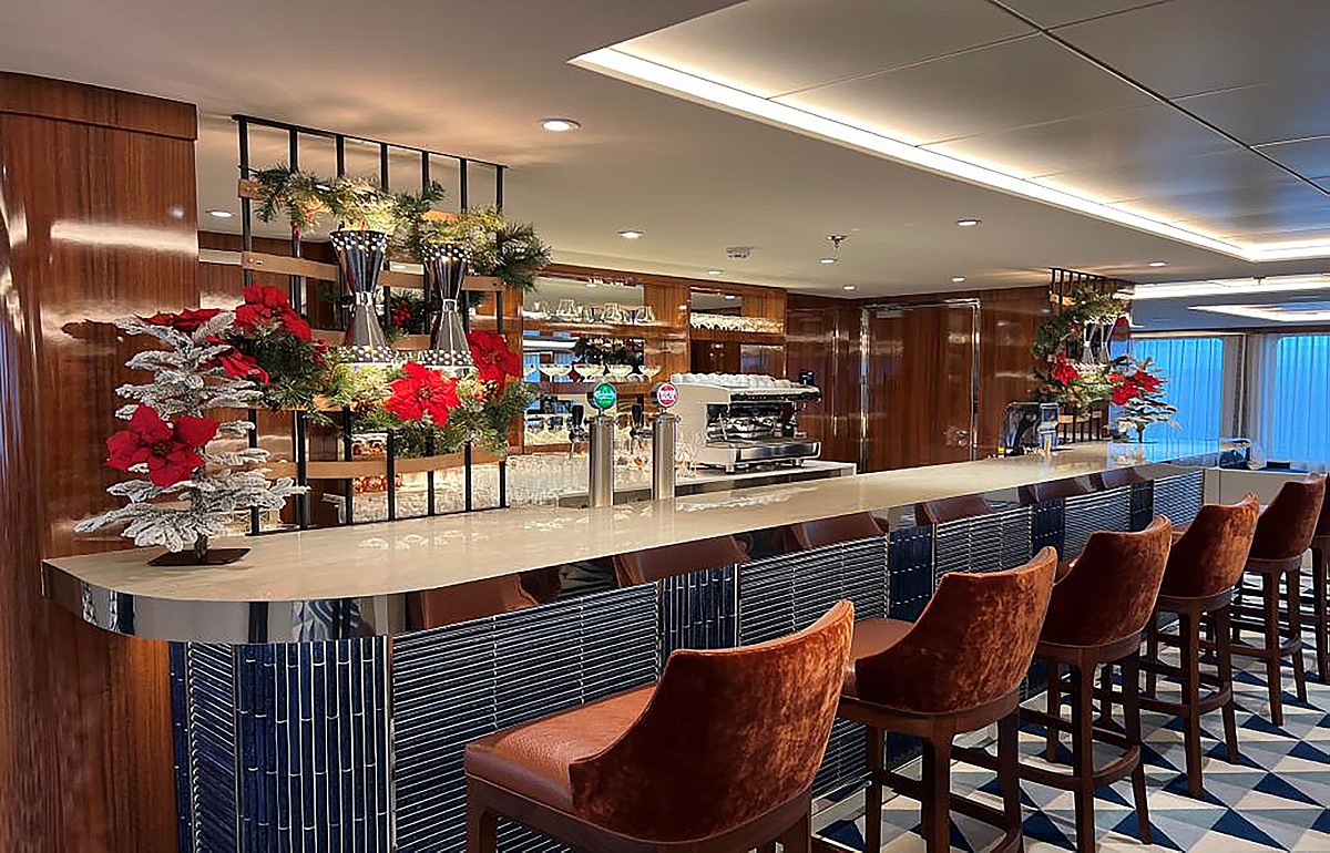 Holiday decorations including red ribbons and garland by a bar on World Traveler cruise ship with Atlas Ocean Voyages.